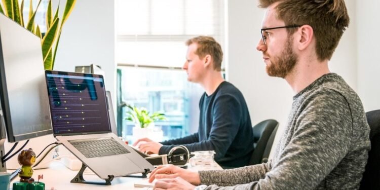 Two men focused on their computers in an office, employing cloud faxing solutions to enhance workflow efficiency.