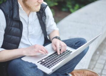 A man seated on a bench, typing on his laptop, exploring AI integration software.