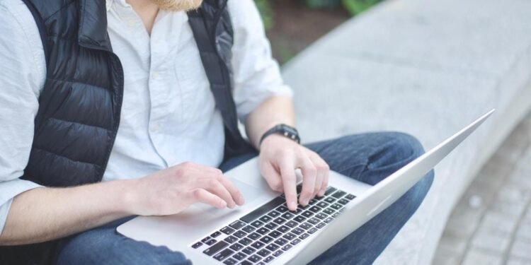A man seated on a bench, typing on his laptop, exploring AI integration software.