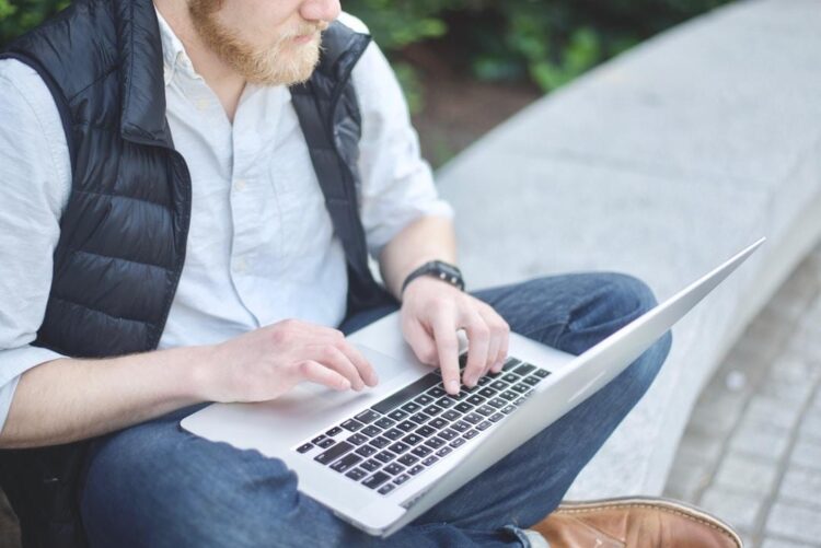 A man seated on a bench, typing on his laptop, exploring AI integration software.
