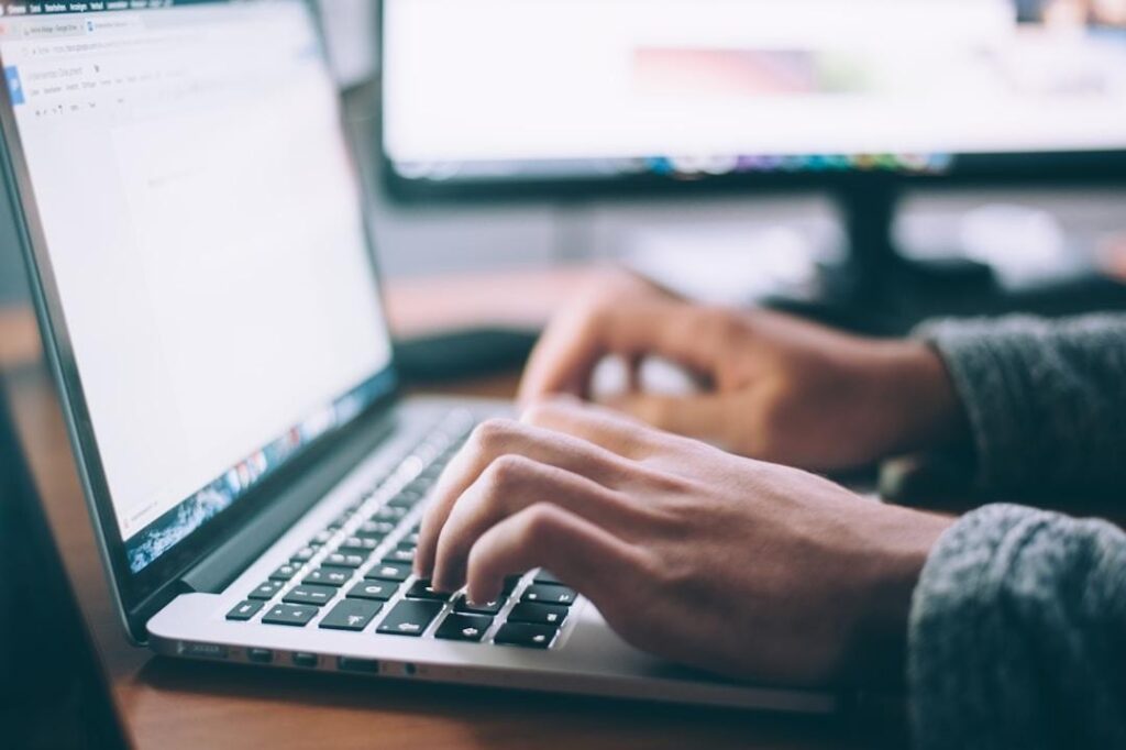 An individual engaged in typing on a laptop, showcasing concentration and the glow of the screen in a workspace.